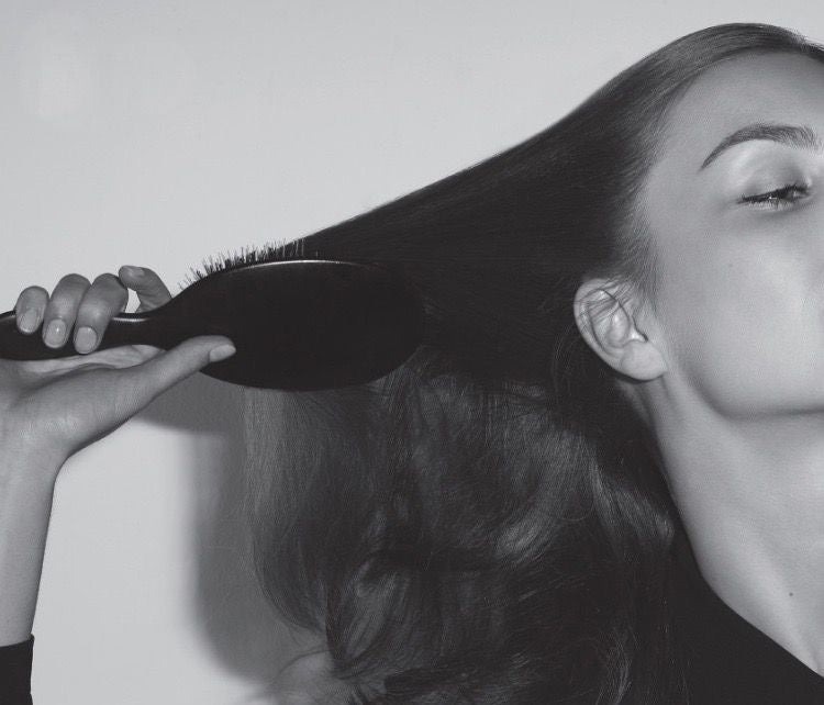 Black and white photo of a woman brushing her long dark hair with a large paddle brush