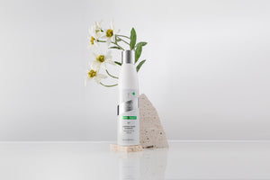 Luminox Shine Shampoo bottle with white flowers and stone on reflective surface, clean minimal background